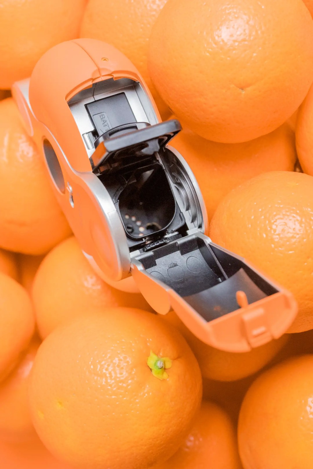 A Canon ELPH Shades Sunshine camera sitting on top of a pile of oranges. 