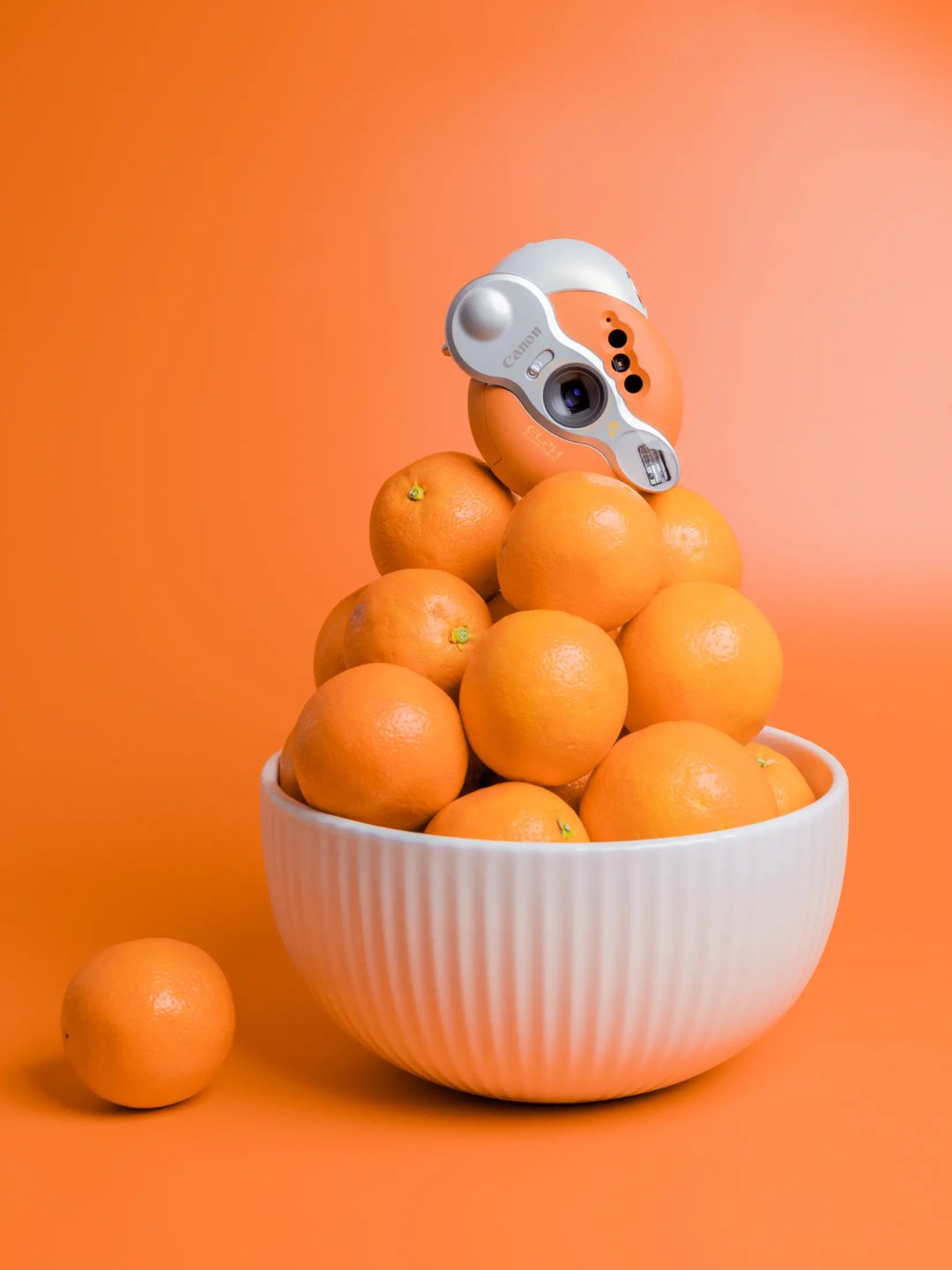 A Canon ELPH Shades Sunshine camera sitting on top of a pile of oranges. 