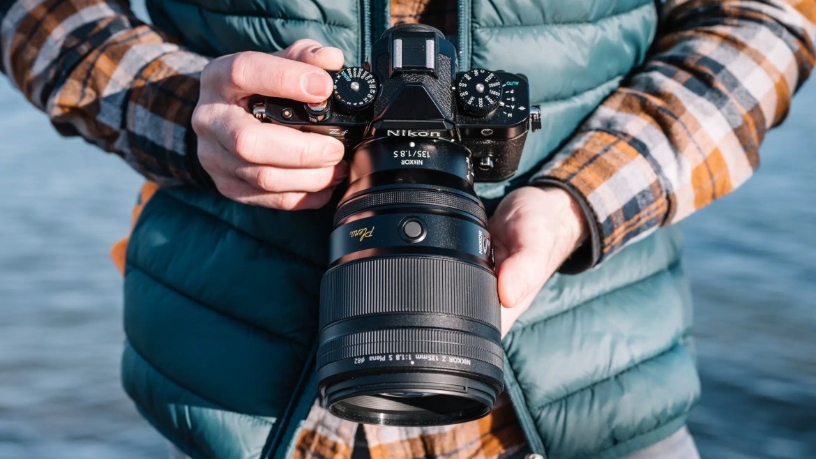 A Nikon Nikkor Z 135mm f/1.8 Plena lens is attached to a Nikon Zf digital mirror-less camera, and the whole kit is being held by a photographer.