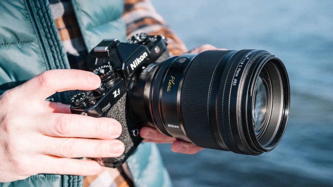 A Nikon Nikkor Z 135mm f/1.8 Plena lens is attached to a Nikon Zf digital mirror-less camera, and the whole kit is being held by a photographer. 